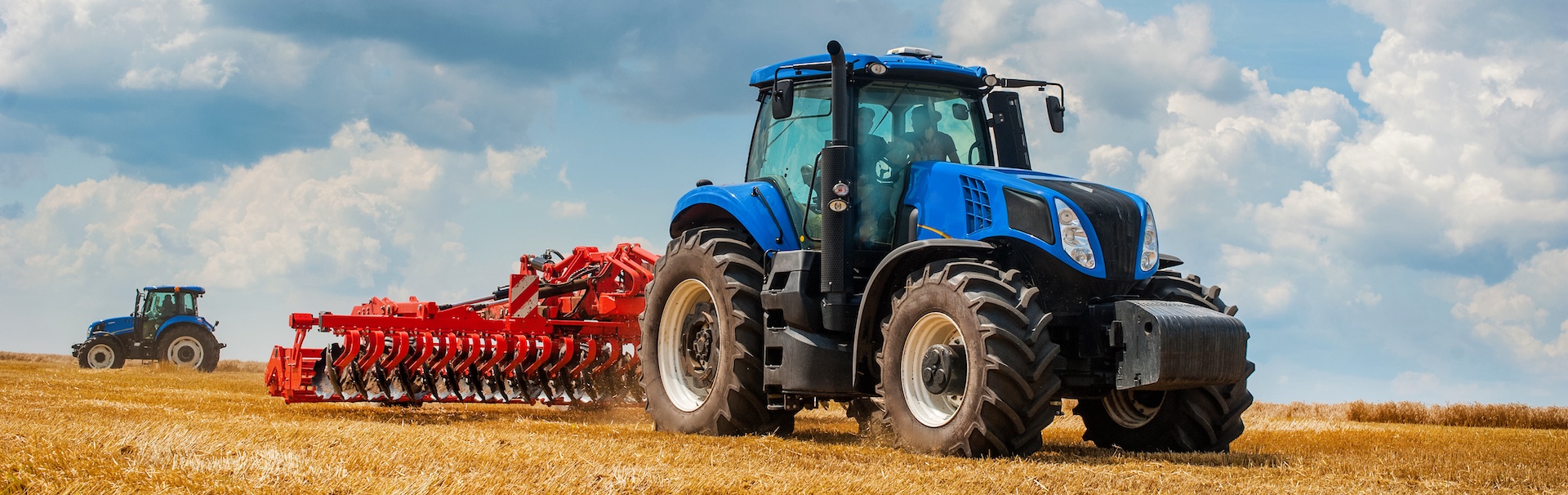 blue new tractor with red harrow in the field against a cloudy sky, agricultural machinery work